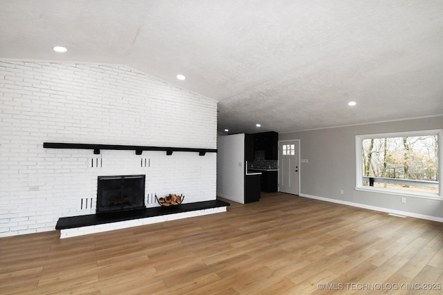 unfurnished living room with brick wall, lofted ceiling, light wood-type flooring, a brick fireplace, and a textured ceiling