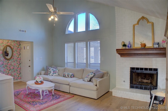 living room with a high ceiling, ceiling fan, hardwood / wood-style floors, and a fireplace