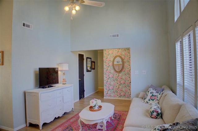 living room with a high ceiling, ceiling fan, and light wood-type flooring