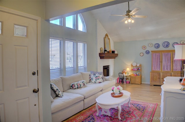 living room with ceiling fan, a fireplace, high vaulted ceiling, and light hardwood / wood-style flooring