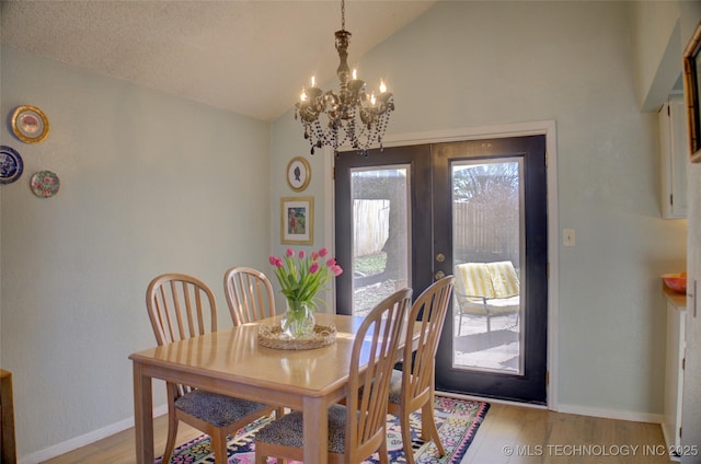 dining space featuring a notable chandelier, vaulted ceiling, french doors, and light wood-type flooring