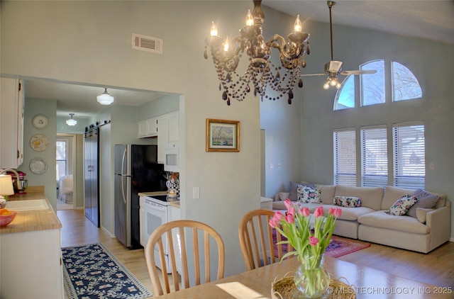 dining space with sink, a high ceiling, ceiling fan, light hardwood / wood-style floors, and a barn door