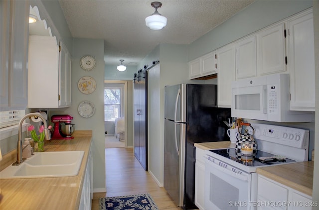 kitchen with white cabinetry, a barn door, sink, and white appliances