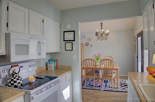 kitchen with white appliances, hanging light fixtures, a notable chandelier, white cabinets, and light wood-type flooring