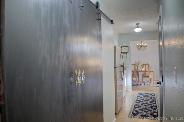 hall featuring a barn door, light hardwood / wood-style floors, a textured ceiling, and a notable chandelier