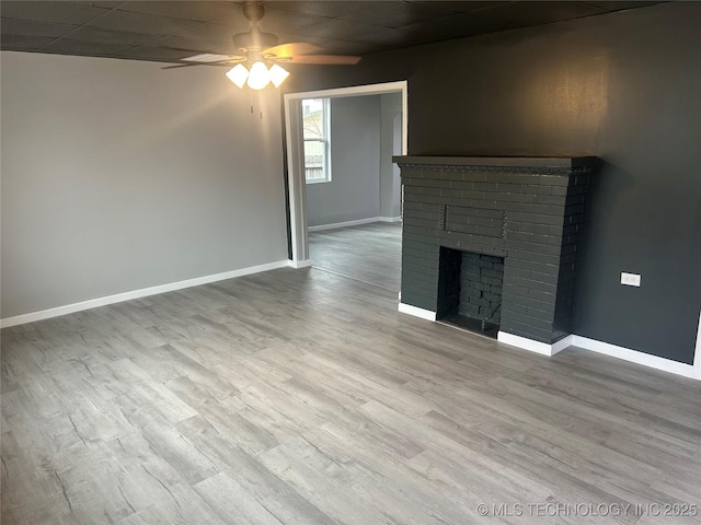 unfurnished living room with ceiling fan, a fireplace, a drop ceiling, and light wood-type flooring