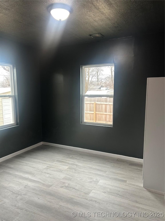 spare room with a textured ceiling, light hardwood / wood-style flooring, and a healthy amount of sunlight