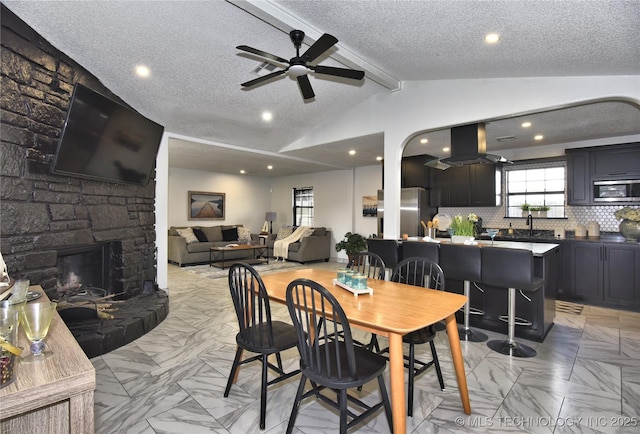 dining space with a fireplace, lofted ceiling with beams, sink, ceiling fan, and a textured ceiling