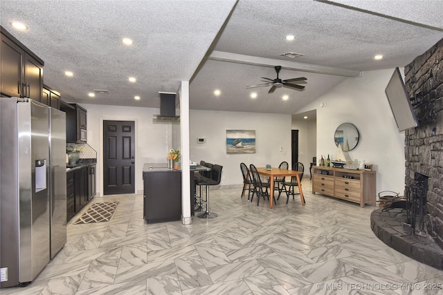 kitchen with stainless steel fridge, ceiling fan, vaulted ceiling with beams, a fireplace, and a textured ceiling