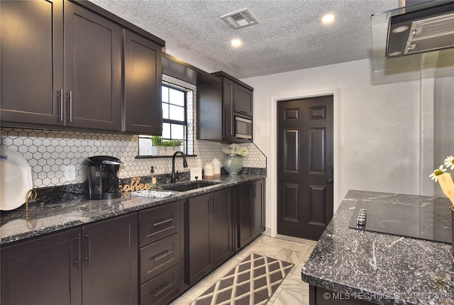 kitchen featuring stainless steel microwave, sink, dark stone countertops, dark brown cabinetry, and black electric cooktop