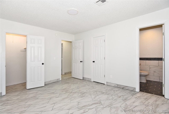 unfurnished bedroom with tile walls, a closet, a textured ceiling, and ensuite bathroom