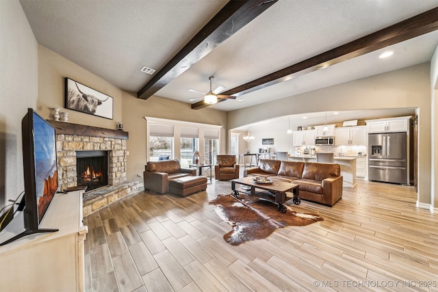 living room with a stone fireplace, vaulted ceiling with beams, a textured ceiling, and ceiling fan