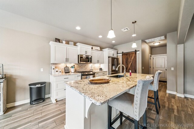 kitchen featuring sink, appliances with stainless steel finishes, an island with sink, a barn door, and white cabinets