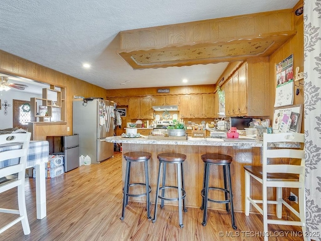 kitchen featuring a breakfast bar area, a textured ceiling, light wood-type flooring, stainless steel refrigerator, and kitchen peninsula