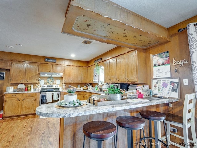 kitchen with stainless steel electric range oven, a kitchen breakfast bar, kitchen peninsula, and light hardwood / wood-style floors