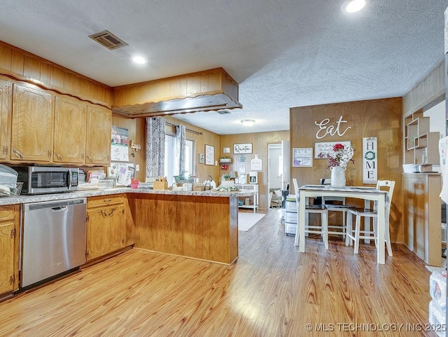 kitchen with stainless steel appliances, kitchen peninsula, a textured ceiling, and light wood-type flooring