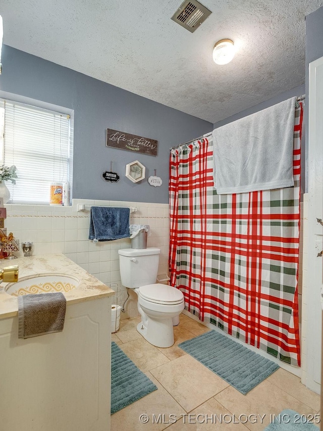 bathroom with tile patterned floors, toilet, sink, a textured ceiling, and tile walls