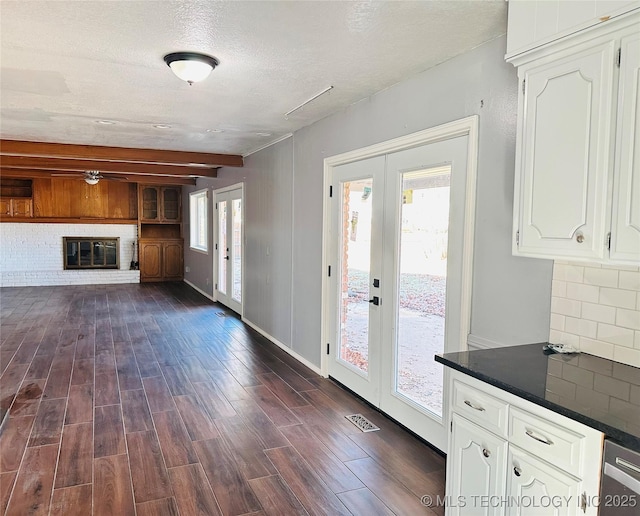 unfurnished living room with beamed ceiling, a brick fireplace, dark wood-type flooring, a textured ceiling, and french doors