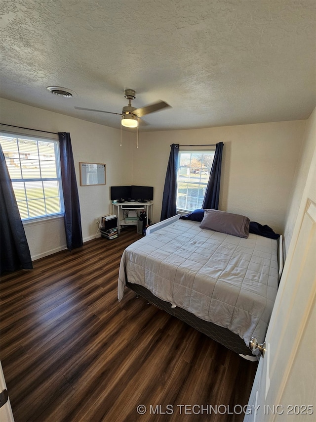 bedroom with a textured ceiling, dark wood-type flooring, and ceiling fan