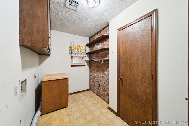 laundry area with cabinets, brick wall, a textured ceiling, washer hookup, and hookup for an electric dryer