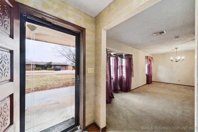 entryway featuring carpet floors, a textured ceiling, and a notable chandelier