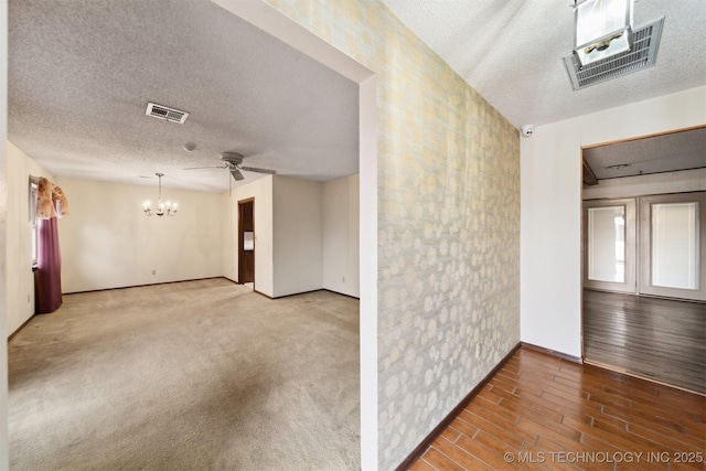 empty room featuring ceiling fan with notable chandelier, hardwood / wood-style floors, and a textured ceiling