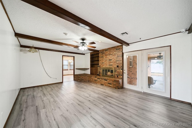 unfurnished living room featuring a healthy amount of sunlight, beam ceiling, light hardwood / wood-style floors, and a textured ceiling