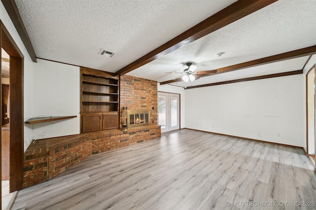 unfurnished living room featuring beam ceiling, light hardwood / wood-style floors, a textured ceiling, a brick fireplace, and built in shelves