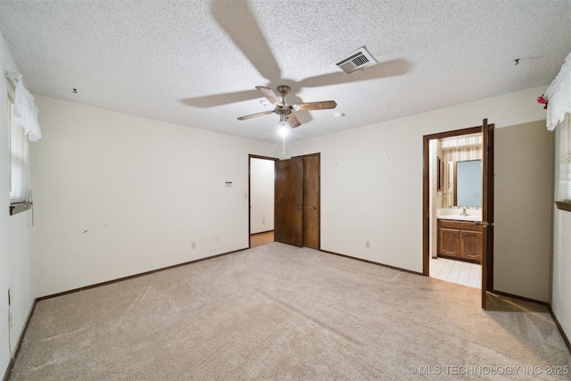 unfurnished bedroom featuring ensuite bath, sink, ceiling fan, light carpet, and a textured ceiling