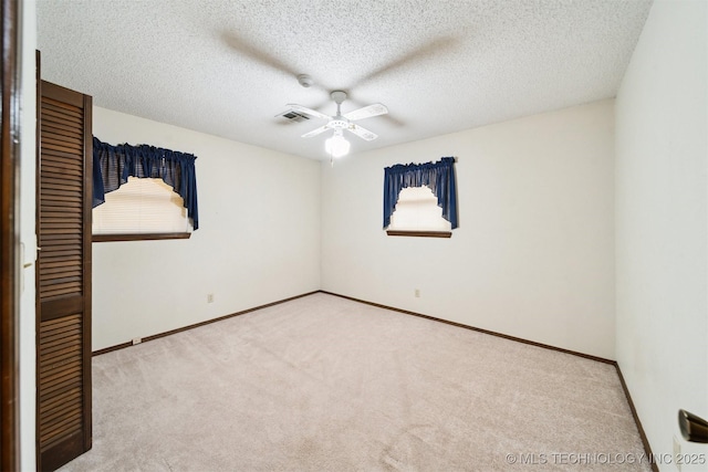 spare room with a textured ceiling, light colored carpet, and ceiling fan