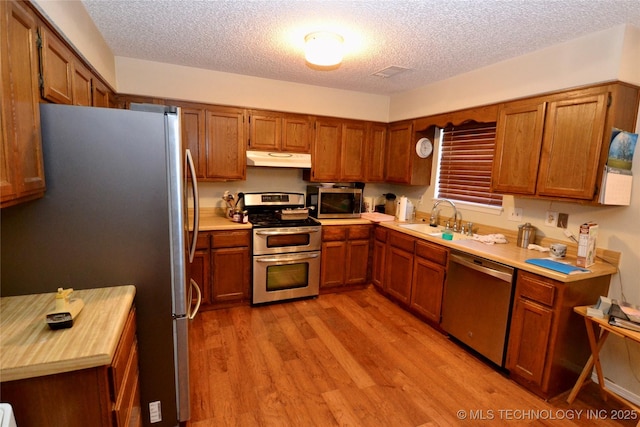 kitchen with sink, stainless steel appliances, a textured ceiling, and light wood-type flooring