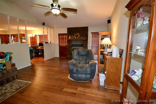 living room with ceiling fan with notable chandelier, a stone fireplace, hardwood / wood-style floors, and lofted ceiling