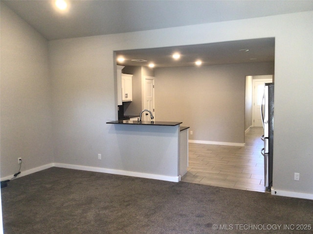 kitchen with stainless steel refrigerator, white cabinetry, carpet floors, sink, and kitchen peninsula