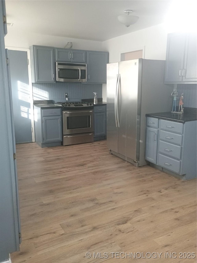 kitchen with gray cabinetry, light hardwood / wood-style flooring, stainless steel appliances, and tasteful backsplash