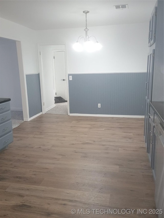 unfurnished dining area with wood-type flooring and an inviting chandelier