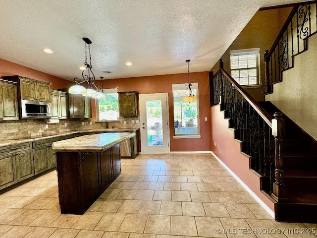 kitchen featuring sink, decorative light fixtures, dark brown cabinets, a kitchen island, and backsplash