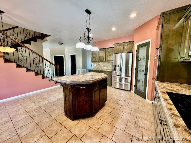 kitchen with backsplash, dark brown cabinets, stainless steel refrigerator with ice dispenser, a kitchen island, and black cooktop