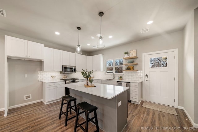 kitchen featuring dark wood-type flooring, appliances with stainless steel finishes, white cabinetry, a kitchen island, and decorative light fixtures