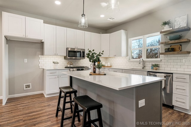 kitchen with a kitchen island, white cabinetry, sink, hanging light fixtures, and stainless steel appliances