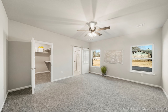 unfurnished bedroom featuring ensuite bathroom, a walk in closet, carpet flooring, a closet, and ceiling fan