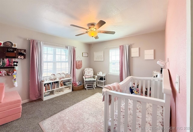 carpeted bedroom featuring a nursery area, ceiling fan, multiple windows, and a textured ceiling