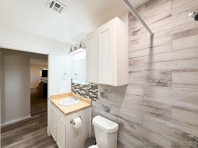 bathroom featuring vanity, wood-type flooring, backsplash, and toilet