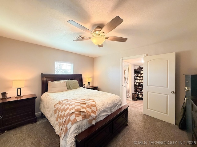 bedroom with ceiling fan, a walk in closet, carpet floors, and a textured ceiling