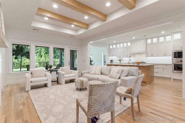 living room featuring sink, beam ceiling, and light hardwood / wood-style flooring