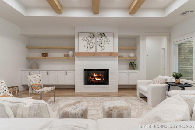 living room with light hardwood / wood-style flooring, a fireplace, built in features, and beamed ceiling