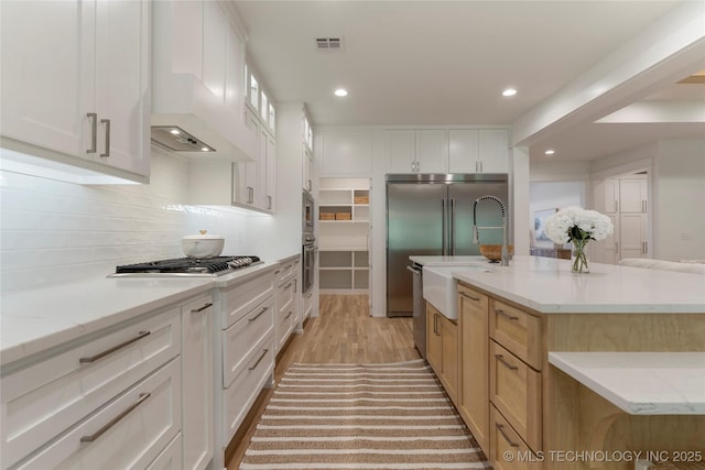 kitchen with a large island with sink, white cabinetry, custom exhaust hood, and stainless steel appliances