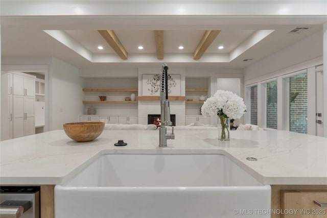 kitchen with a kitchen island, light stone countertops, sink, and beam ceiling