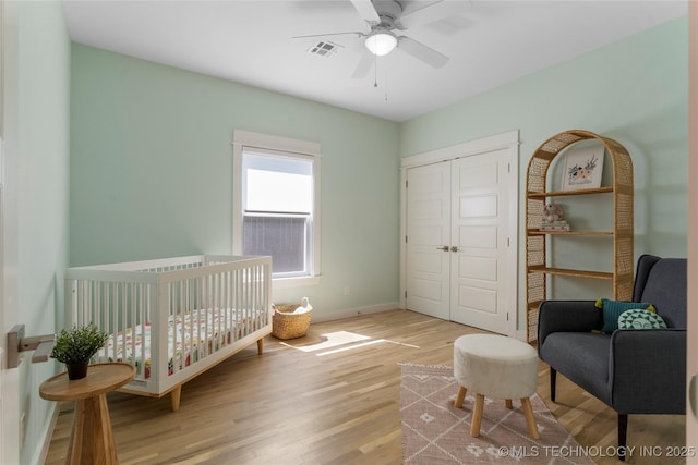 bedroom with ceiling fan, a closet, a nursery area, and light hardwood / wood-style flooring