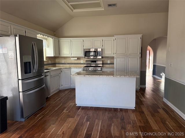 kitchen featuring white cabinetry, light stone counters, vaulted ceiling, appliances with stainless steel finishes, and a kitchen island