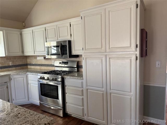 kitchen with lofted ceiling, white cabinets, decorative backsplash, stainless steel appliances, and light stone countertops